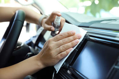 Photo of Woman cleaning dashboard with wet wipe and antibacterial spray in car, closeup