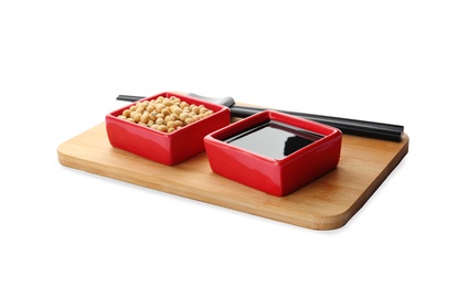 Wooden board with dishes of soy sauce and beans on white background