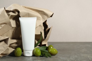 Photo of Tube of cream with olive essential oil and kraft crumpled paper on dark grey table. Space for text