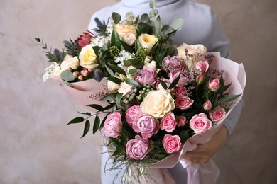 Photo of Woman with bouquets of beautiful flowers on beige background, closeup