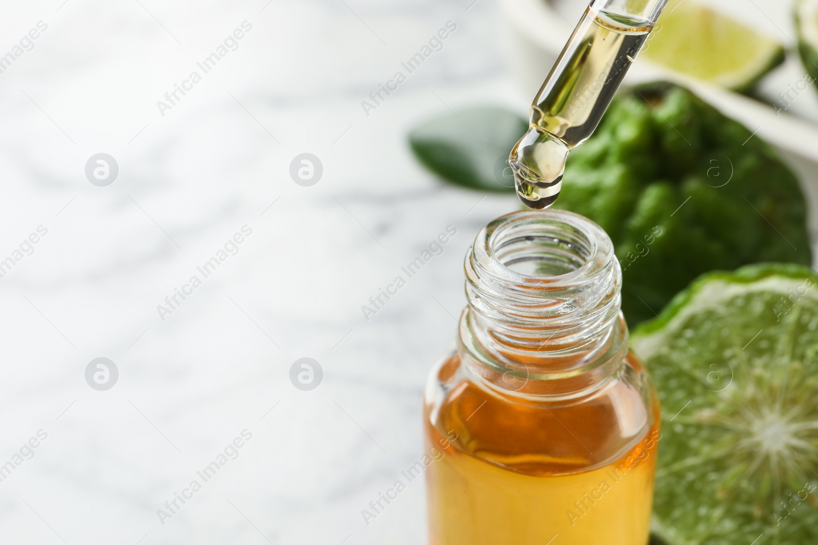 Photo of Bergamot essential oil dripping from pipette into bottle on table, closeup. Space for text