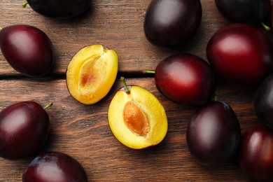 Photo of Tasty ripe plums on wooden table, flat lay