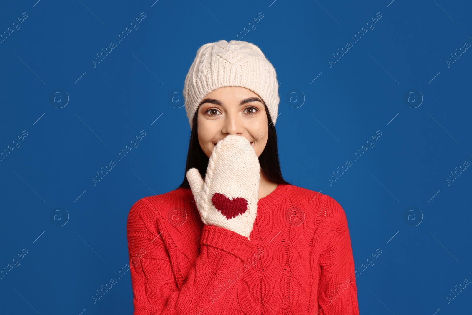 Photo of Young woman wearing warm sweater, mittens and hat on blue background. Winter season