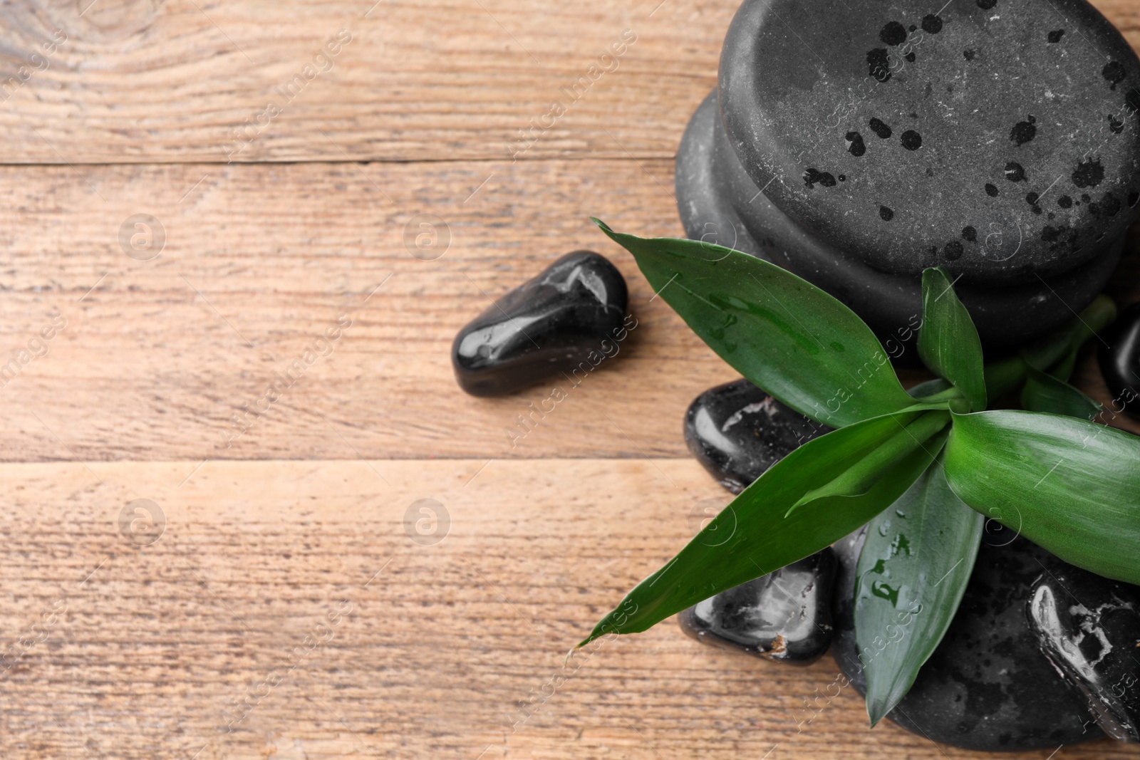 Photo of Wet spa stones and bamboo leaves on wooden table, above view. Space for text