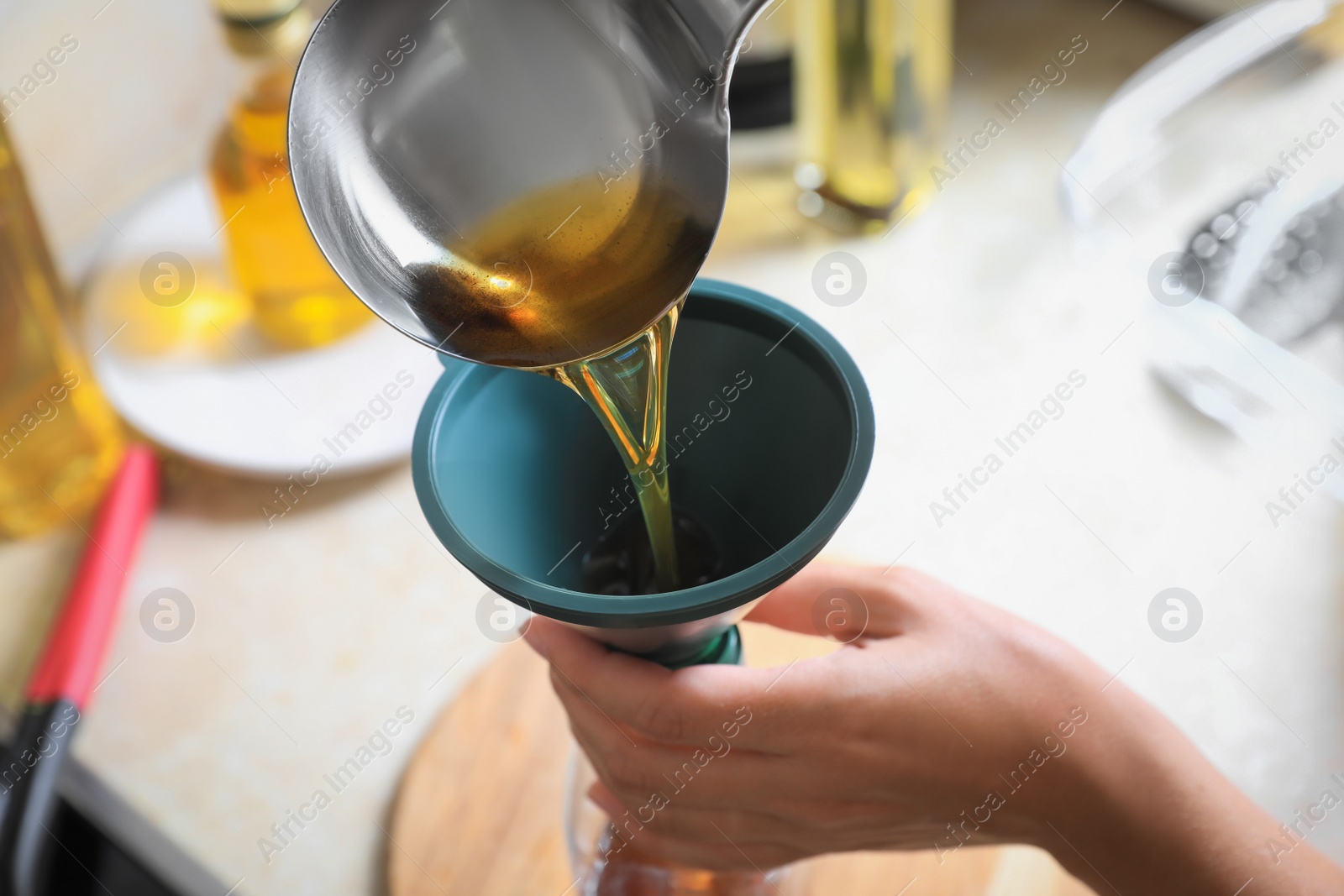 Photo of Woman pouring used cooking oil into bottle through funnel in kitchen, closeup