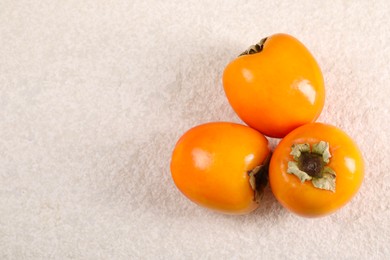 Photo of Delicious ripe persimmons on light textured table, top view. Space for text