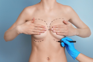 Doctor drawing marks on female breast for cosmetic surgery operation against color background