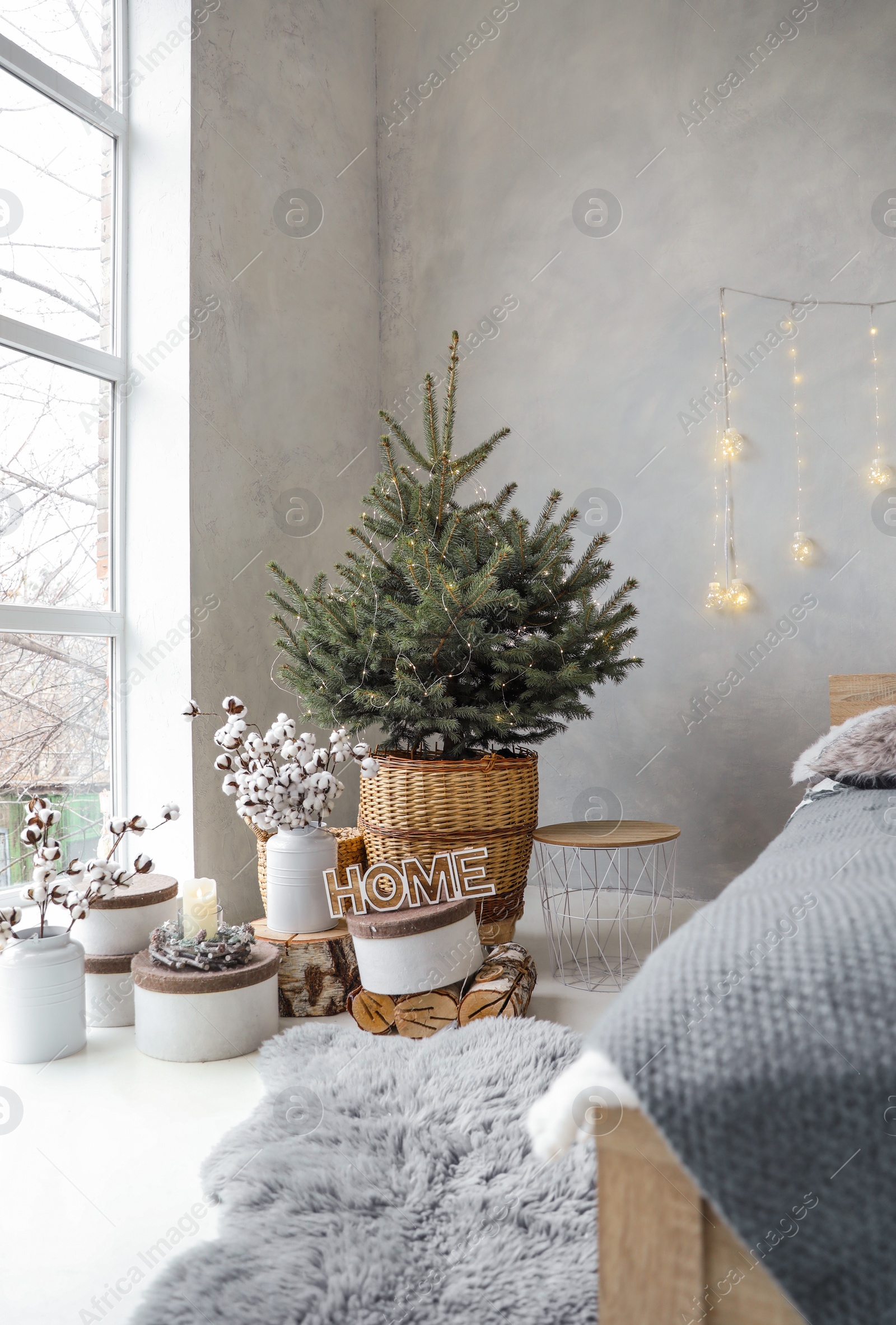 Photo of Little Christmas tree with fairy lights in bedroom interior