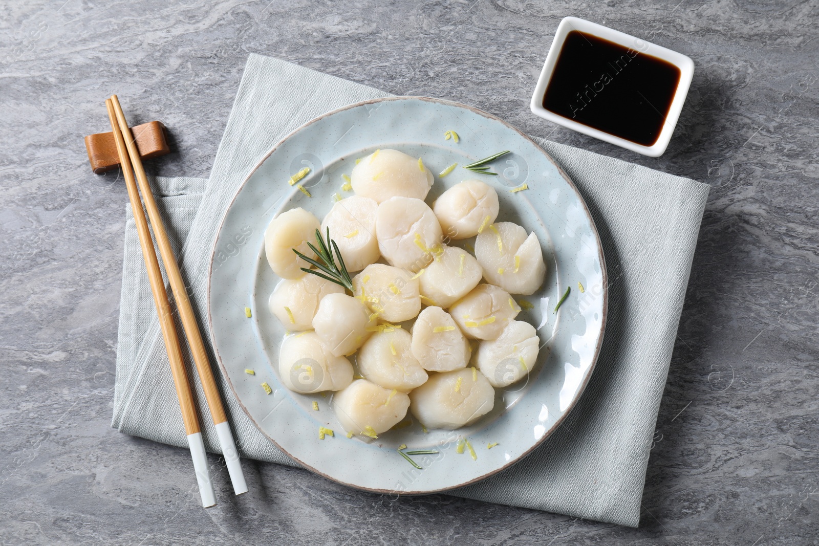 Photo of Raw scallops with lemon zest, rosemary and soy sauce on grey marble table, flat lay