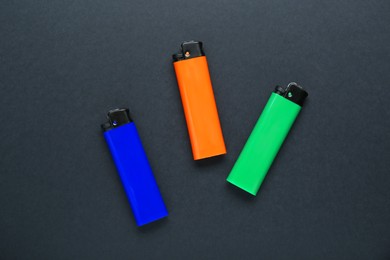 Stylish small pocket lighters on black background, flat lay