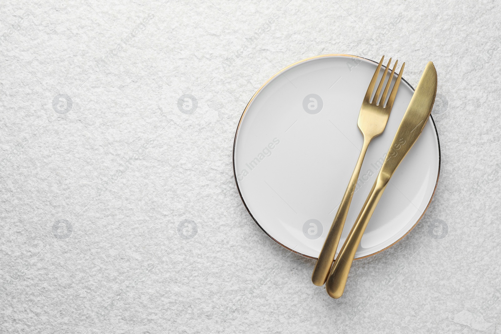 Photo of Stylish setting with cutlery and plate on light textured table, top view. Space for text