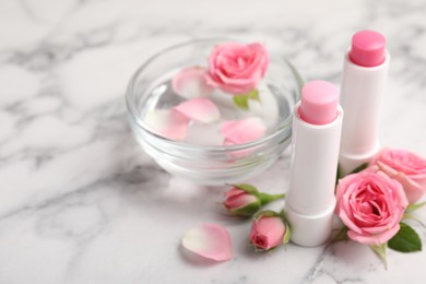 Lip balms, bowl with water and roses on white marble table, closeup