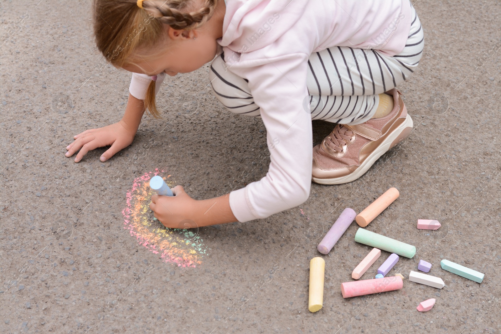 Photo of Little child drawing rainbow with chalk on asphalt