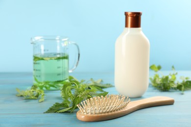 Photo of Stinging nettle, cosmetic product and brush on light blue wooden background. Natural hair care
