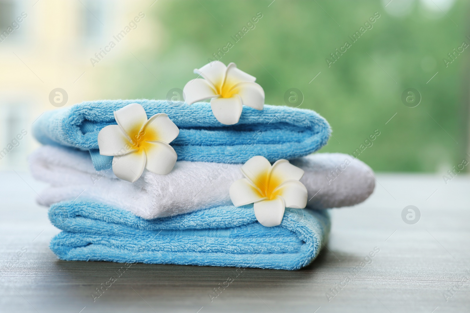 Photo of Pile of fresh towels and flowers on table against blurred background, space for text