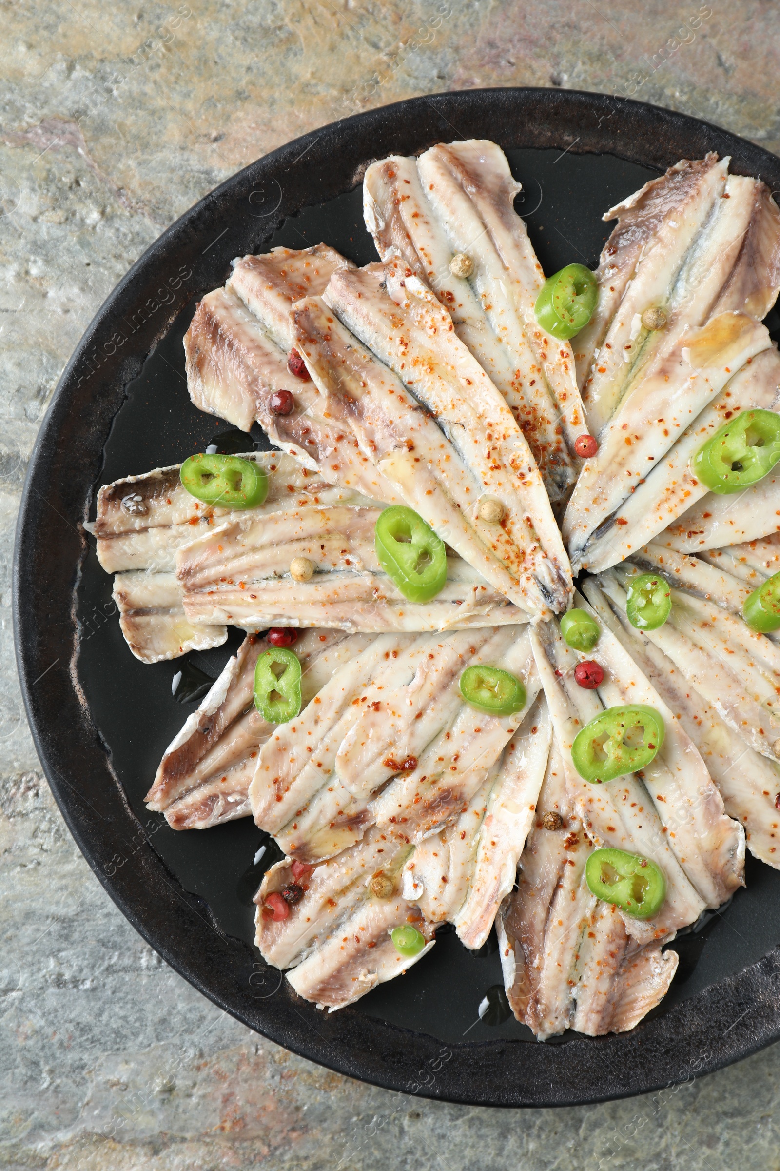 Photo of Tasty pickled anchovies with spices on textured table, top view