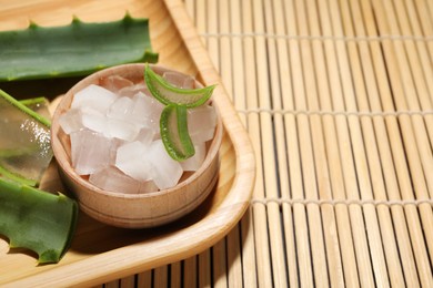 Photo of Aloe vera gel and slices of plant on bamboo mat, closeup. Space for text