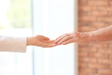 Photo of Young woman holding elderly man hand indoors, closeup. Help service