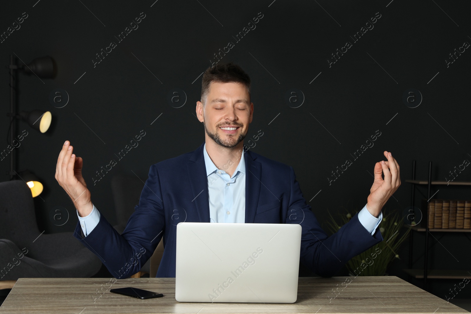 Photo of Businessman practicing zen yoga at table in office