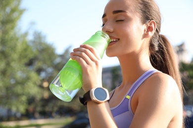Photo of Woman with fitness tracker drinking water after training outdoors