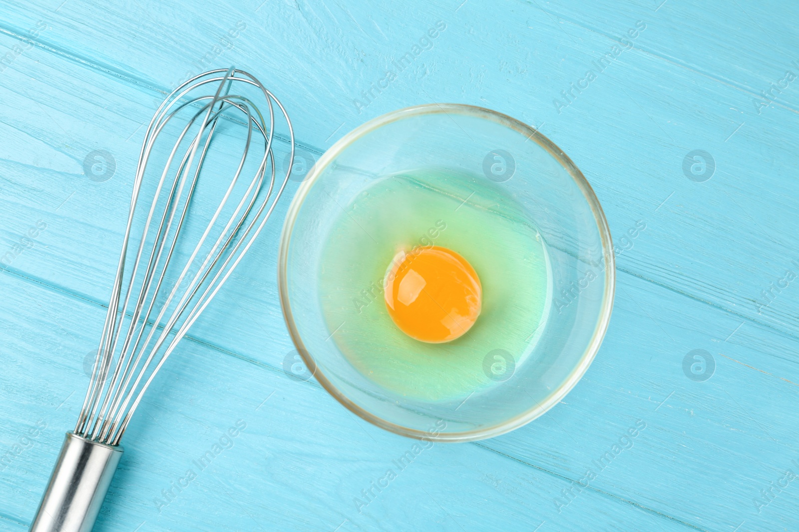 Photo of Raw egg and whisk on light blue wooden table, flat lay. Baking pie