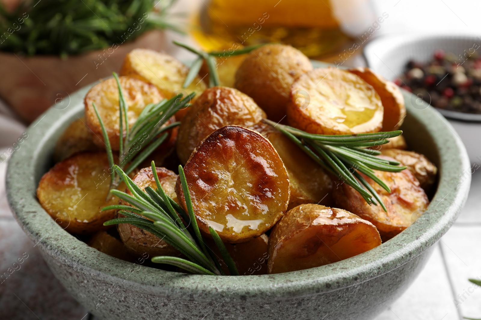 Tasty baked potato and aromatic rosemary in bowl on table, closeup Photo of Tasty baked potato and aromatic rosemary in bowl on table, closeup