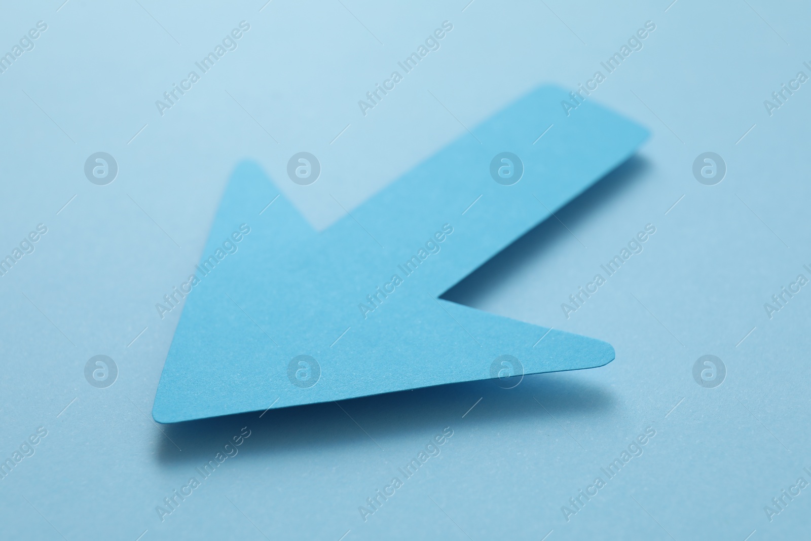 Photo of One paper arrow on light blue background, closeup