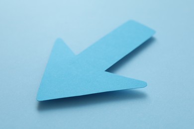 Photo of One paper arrow on light blue background, closeup