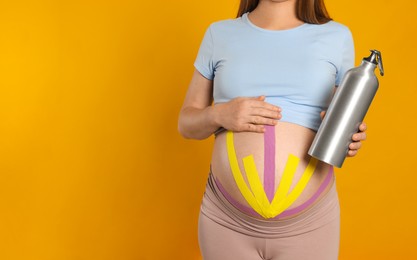 Photo of Pregnant woman with kinesio tapes holding water bottle on orange background, closeup. Space for text