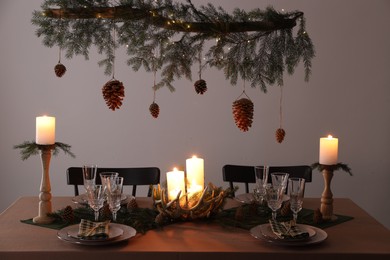 Christmas celebration. Cones hanging from fir tree branch over table with burning candles and tableware