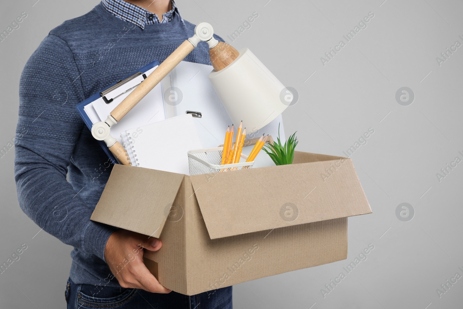 Photo of Unemployed man with box of personal office belongings on light grey background, closeup