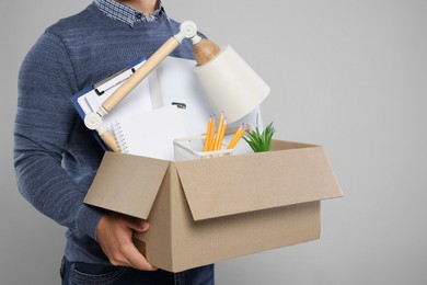 Photo of Unemployed man with box of personal office belongings on light grey background, closeup