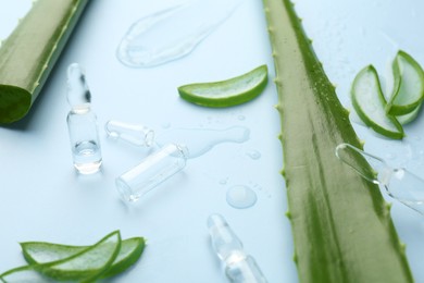 Photo of Skincare ampoules with extract of aloe vera and green leaves on light blue background, closeup