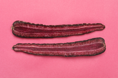 Halves of raw purple carrot on pink background, flat lay