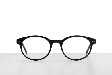 Stylish glasses with black frame on table against white background