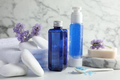 Spa composition. Bottles of cosmetic products, sea salt, stones, soap and flowers on white table