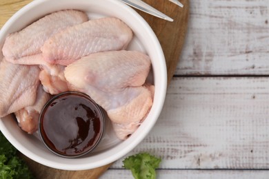 Fresh marinade and raw chicken wings on rustic wooden table, top view. Space for text