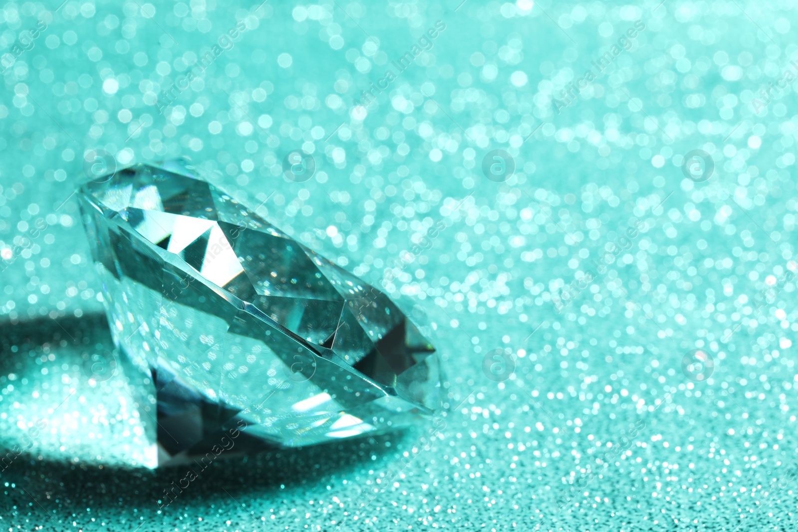 Photo of Beautiful dazzling diamond on green glitter background, closeup. Space for text