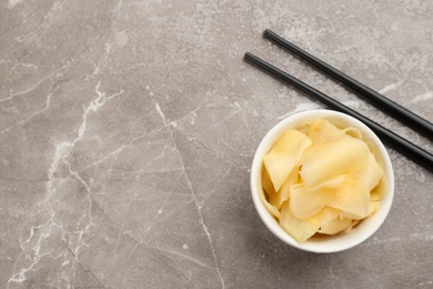 Spicy pickled ginger and chopsticks on grey table, flat lay. Space for text