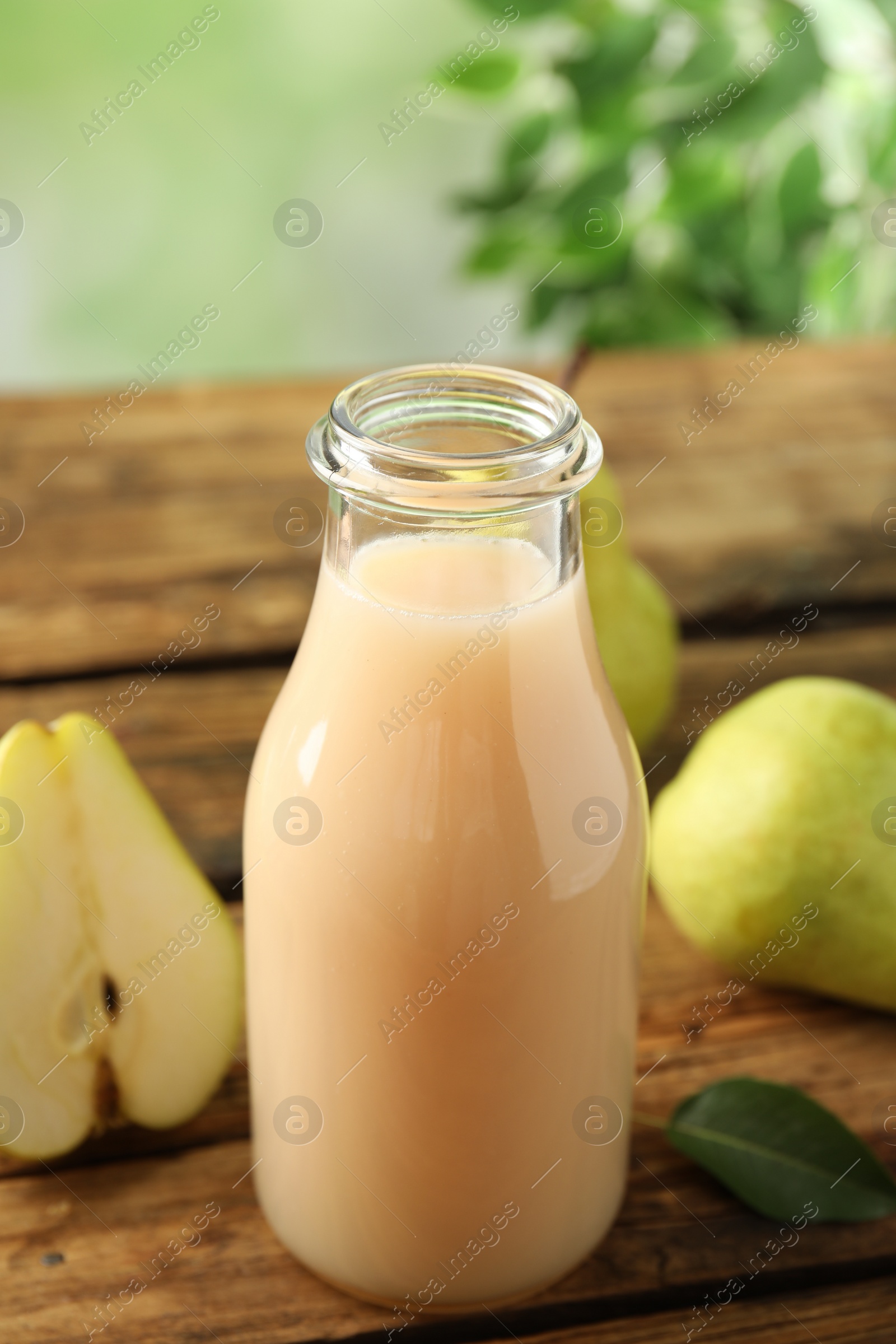 Photo of Fresh pear juice in glass bottle and fruits on wooden table, closeup