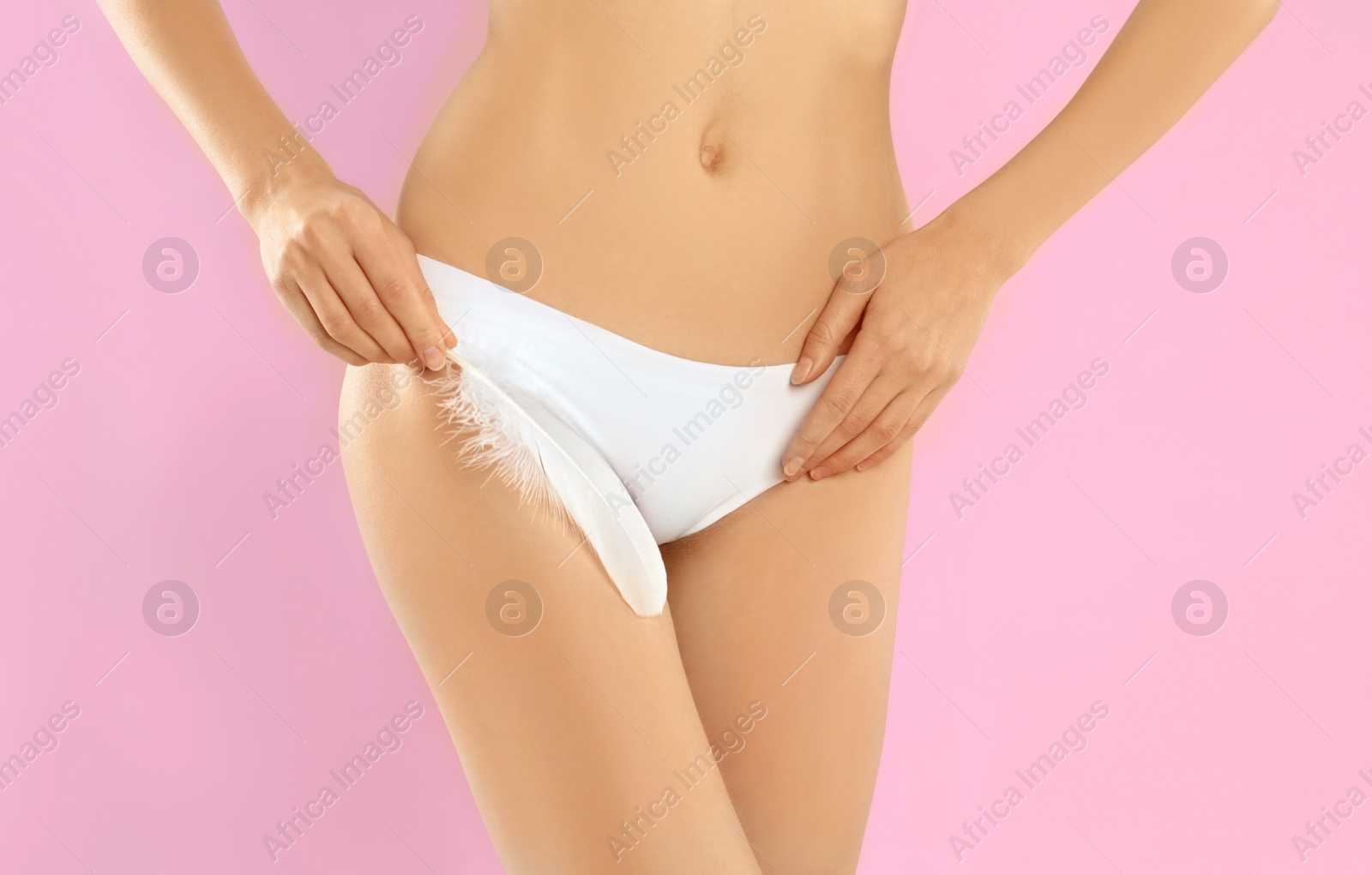 Photo of Woman with feather showing smooth skin after bikini epilation on pink background, closeup. Body care concept
