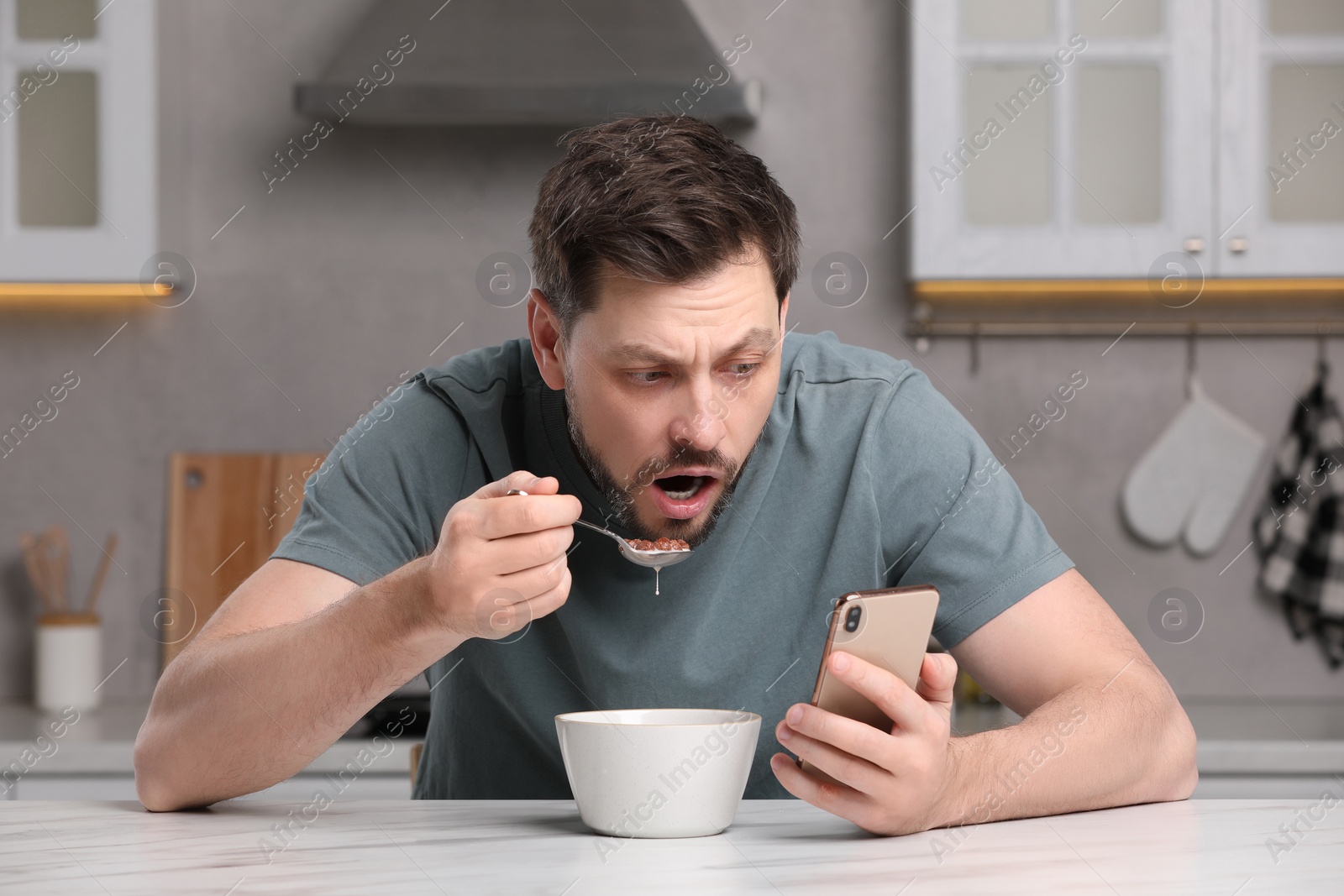 Photo of Man using smartphone while having breakfast at table in kitchen. Internet addiction