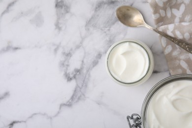 Photo of Delicious natural yogurt in jars and spoon on white marble table, top view, Space for text