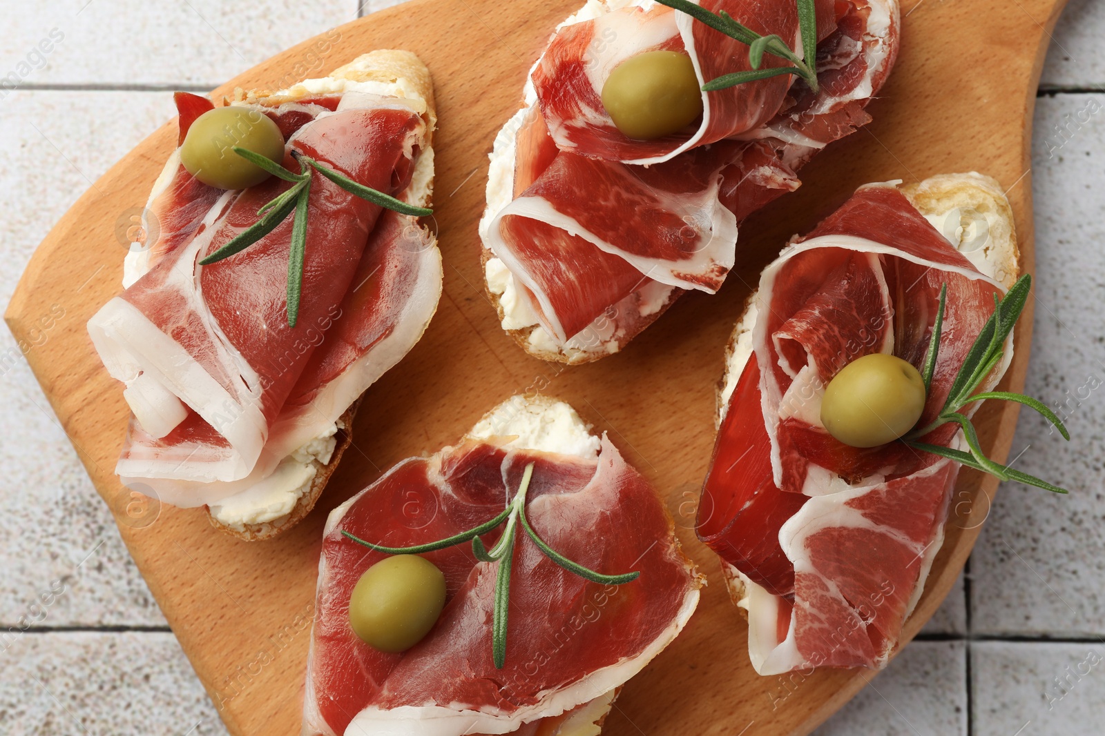 Photo of Tasty sandwiches with cured ham, rosemary and olives on tiled table, top view