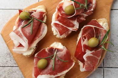 Tasty sandwiches with cured ham, rosemary and olives on tiled table, top view