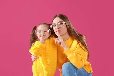 Photo of Young mother and little daughter with glasses on pink background
