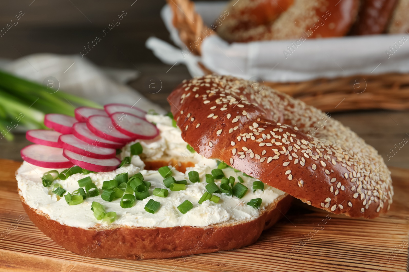 Photo of Delicious bagel with cream cheese, radish and green onion on wooden board, closeup