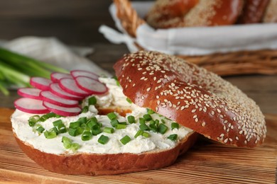 Photo of Delicious bagel with cream cheese, radish and green onion on wooden board, closeup