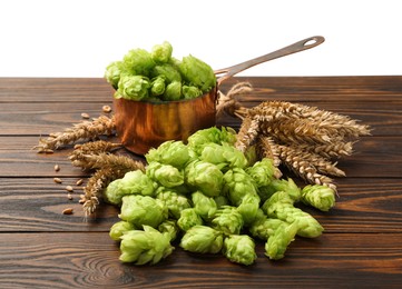 Photo of Fresh hop flowers and wheat ears on wooden table against white background
