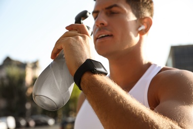 Man with fitness tracker drinking water after training outdoors, closeup